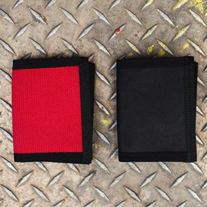 Two bifold wallets, one red and one black, on a textured metal surface.