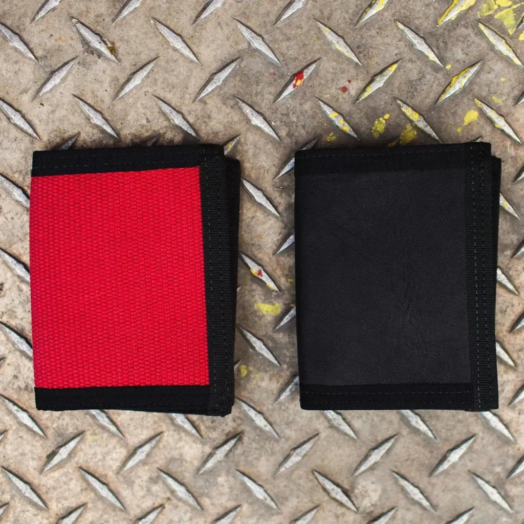 Two bi-fold wallets, one red canvas and one black, on a textured metal surface.