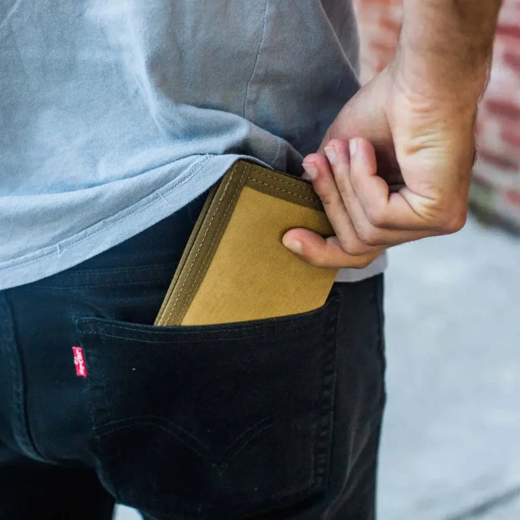 A tan Hypalon wallet being placed into the back pocket of black jeans.