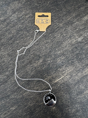 Silver mountain necklace with sun pendant, handmade tag visible, on a dark wood surface. 16 inch chain.