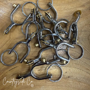 Silver western spur keychains with gold accents on a wooden surface.