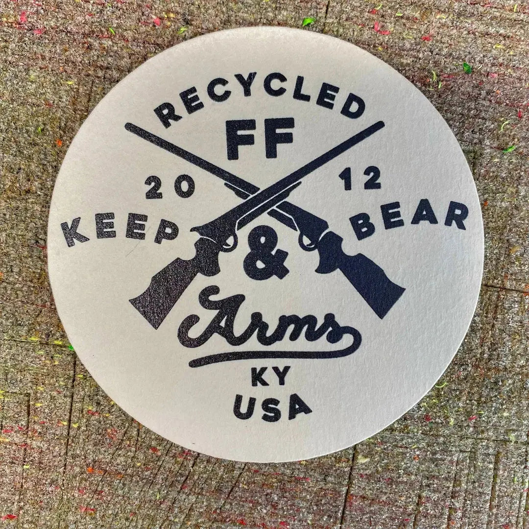 Round coaster with crossed rifles and text RECYCLED FF KEEP & ARMS.