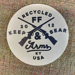 Round coaster with crossed rifles and text RECYCLED FF KEEP & ARMS.