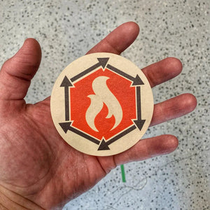 Round coaster with hexagonal border, flame symbol, and surrounding arrows.