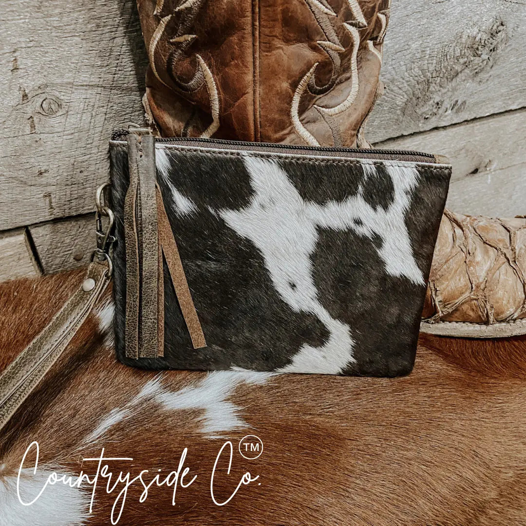 Cowhide wristlet with leather trim and fringe detail, featuring a spotted pattern.