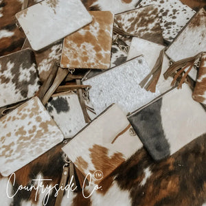 Cowhide leather wristlet with fringe detail and zipper closure shown in a pile.