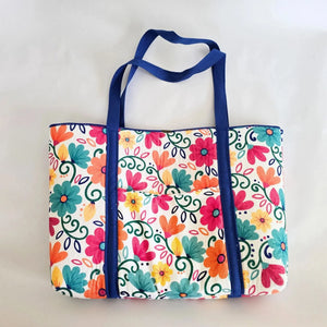 Colorful floral tote bag with blue straps and a front pocket on a white background.