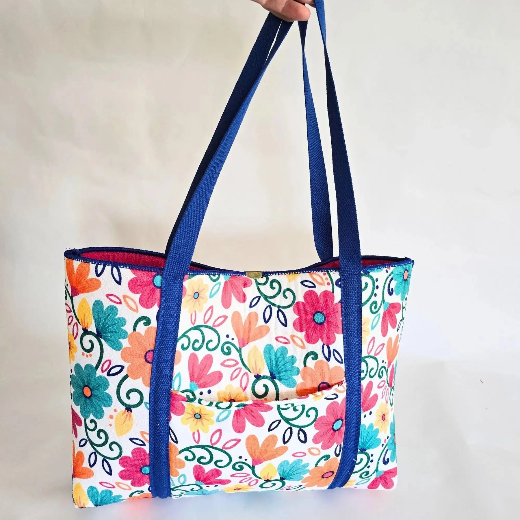 Colorful floral tote bag with blue straps and a front pocket, open top.