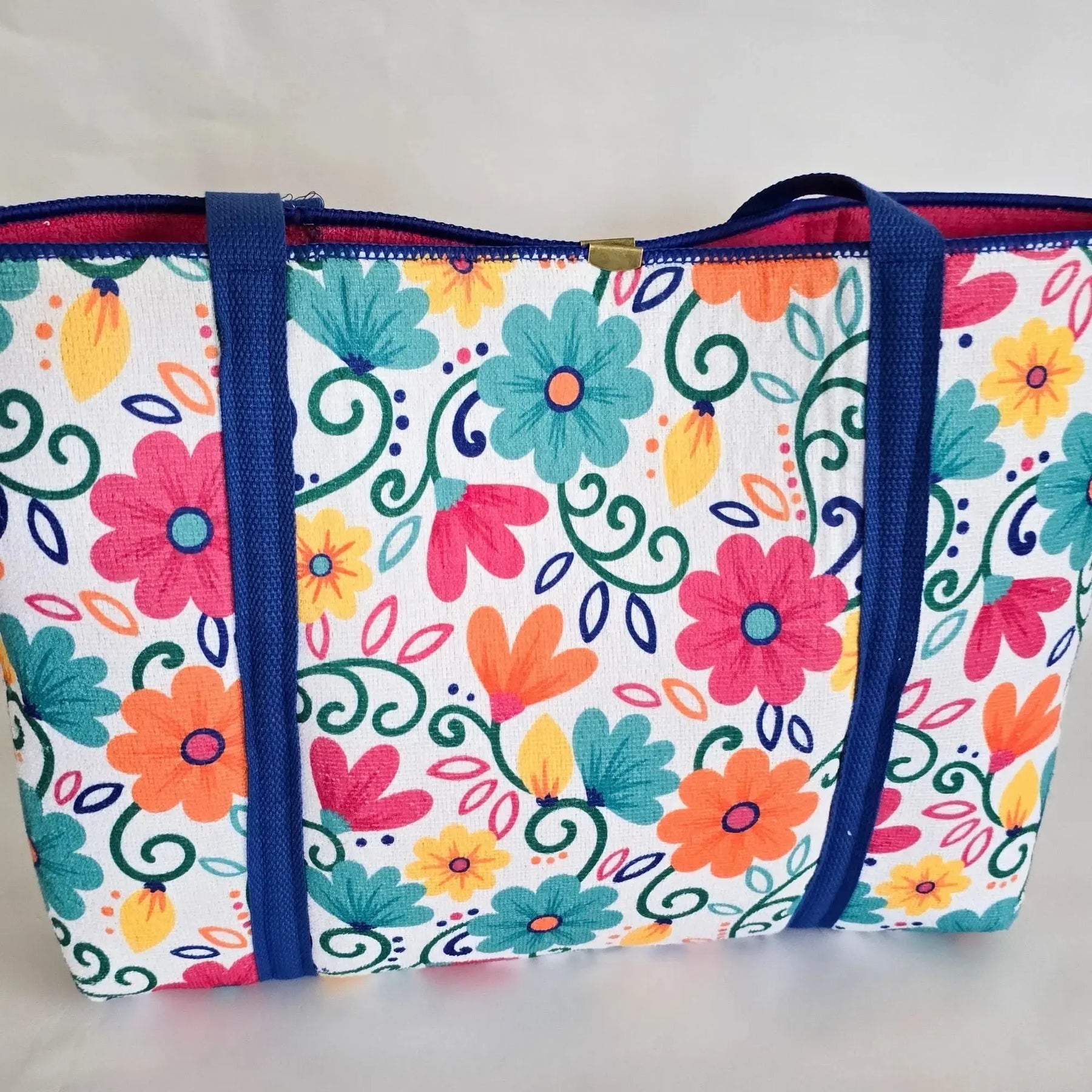 Colorful floral tote bag with blue straps on a white background.