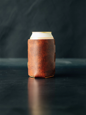 Cognac leather can cooler with a white can inside on a dark surface. Coozie with Loyal Stricklin logo on bottom.