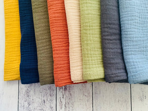 Set of eight cotton crinkle cloth napkins in yellow, navy, olive, rust, cream, green, grey, and blue.