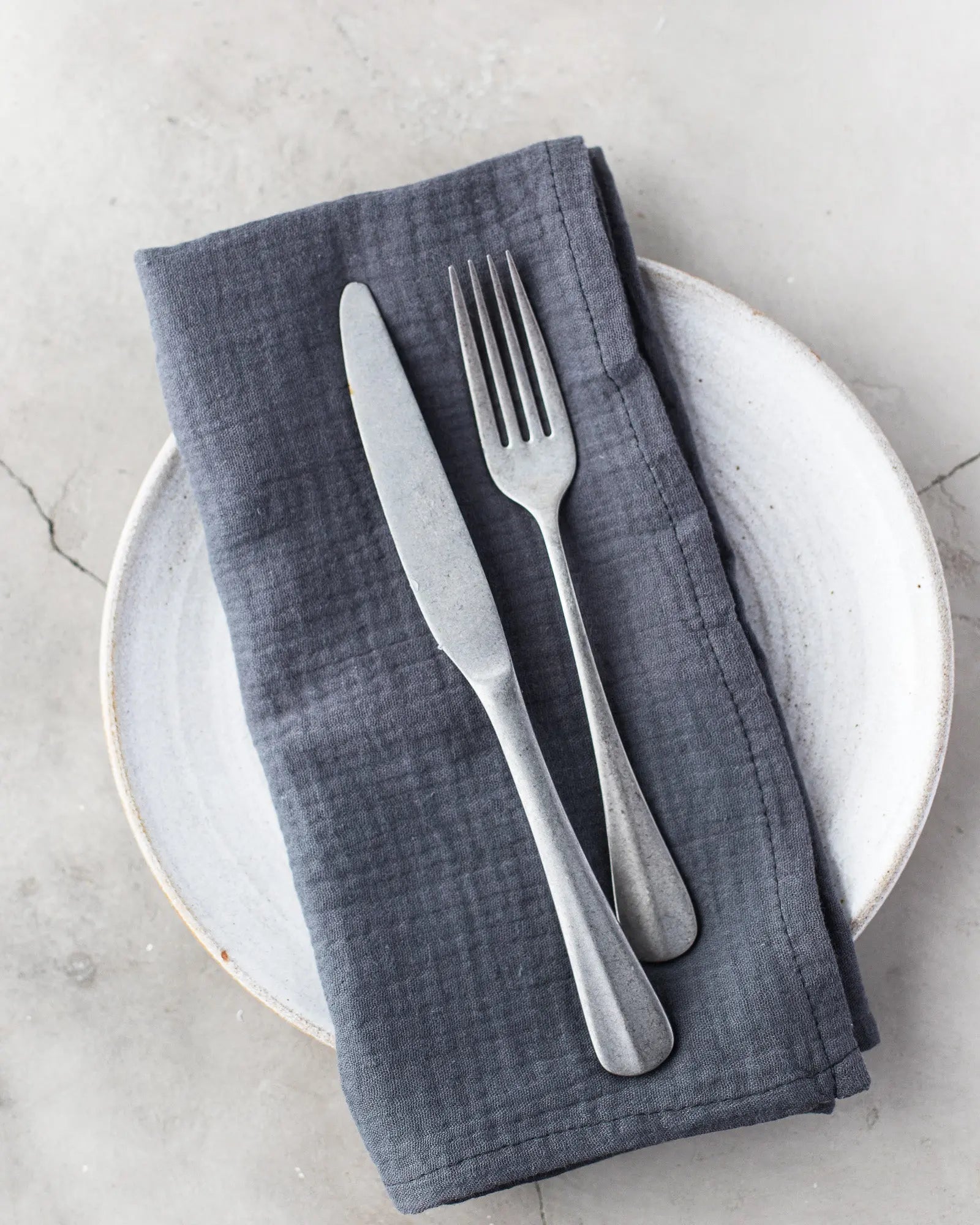 Set of four dark gray cotton crinkle cloth napkins on a plate with a fork and knife.