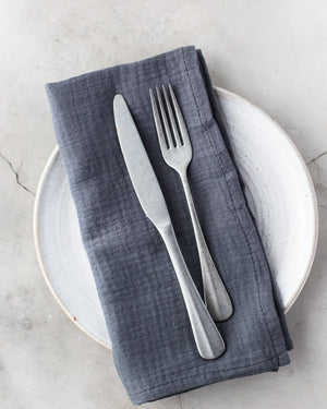 Set of four dark gray cotton crinkle cloth napkins on a plate with a fork and knife.