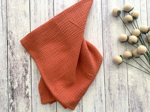 Burnt orange cotton crinkle cloth napkins arranged on a light wooden surface.