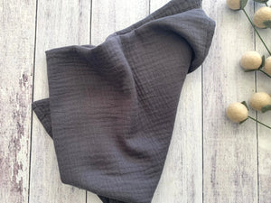 Dark grey cotton crinkle cloth napkins folded on a white wooden background.