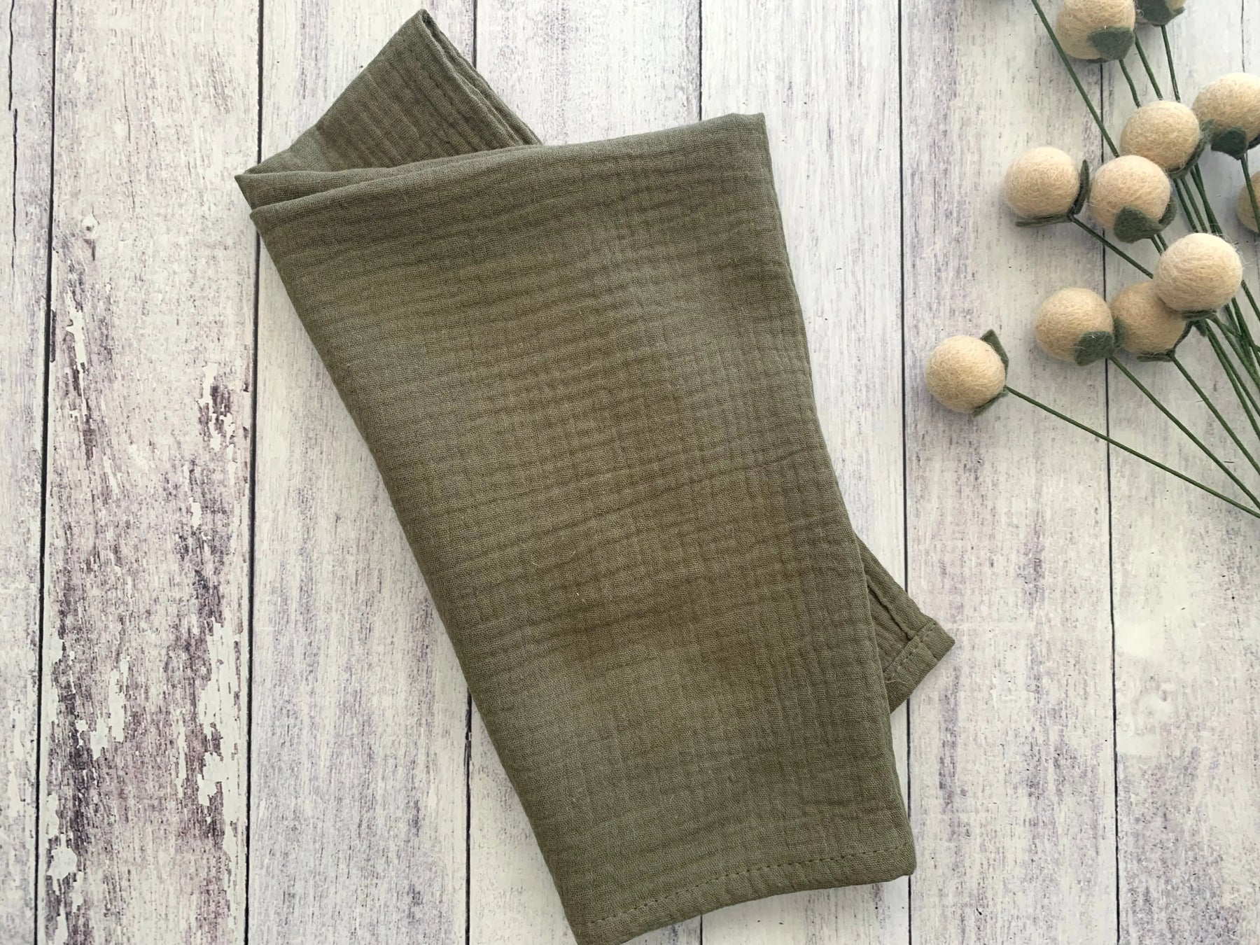 Folded olive green crinkle cloth napkins on a distressed white wood background.