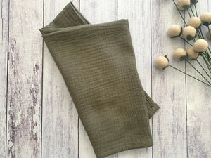 Folded olive green crinkle cloth napkins on a distressed white wood background.