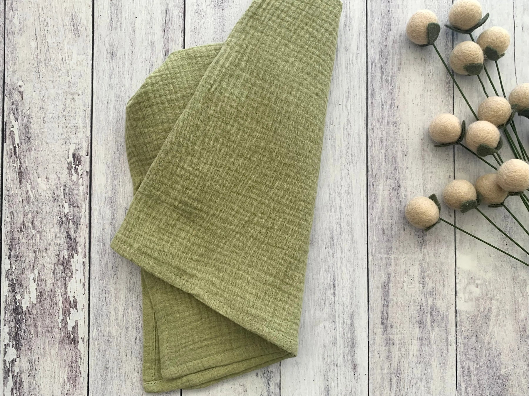 Green cotton crinkle cloth napkins folded on a white wooden background