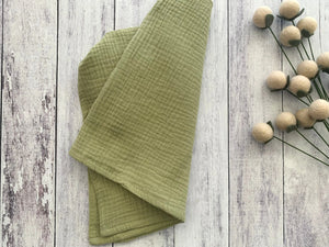 Green cotton crinkle cloth napkins folded on a white wooden background