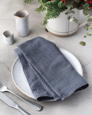 Dark gray cotton crinkle napkins folded on a white plate with silverware.