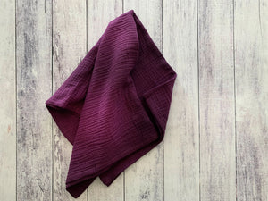 Plum colored crinkle cloth napkin folded on a distressed wood background.