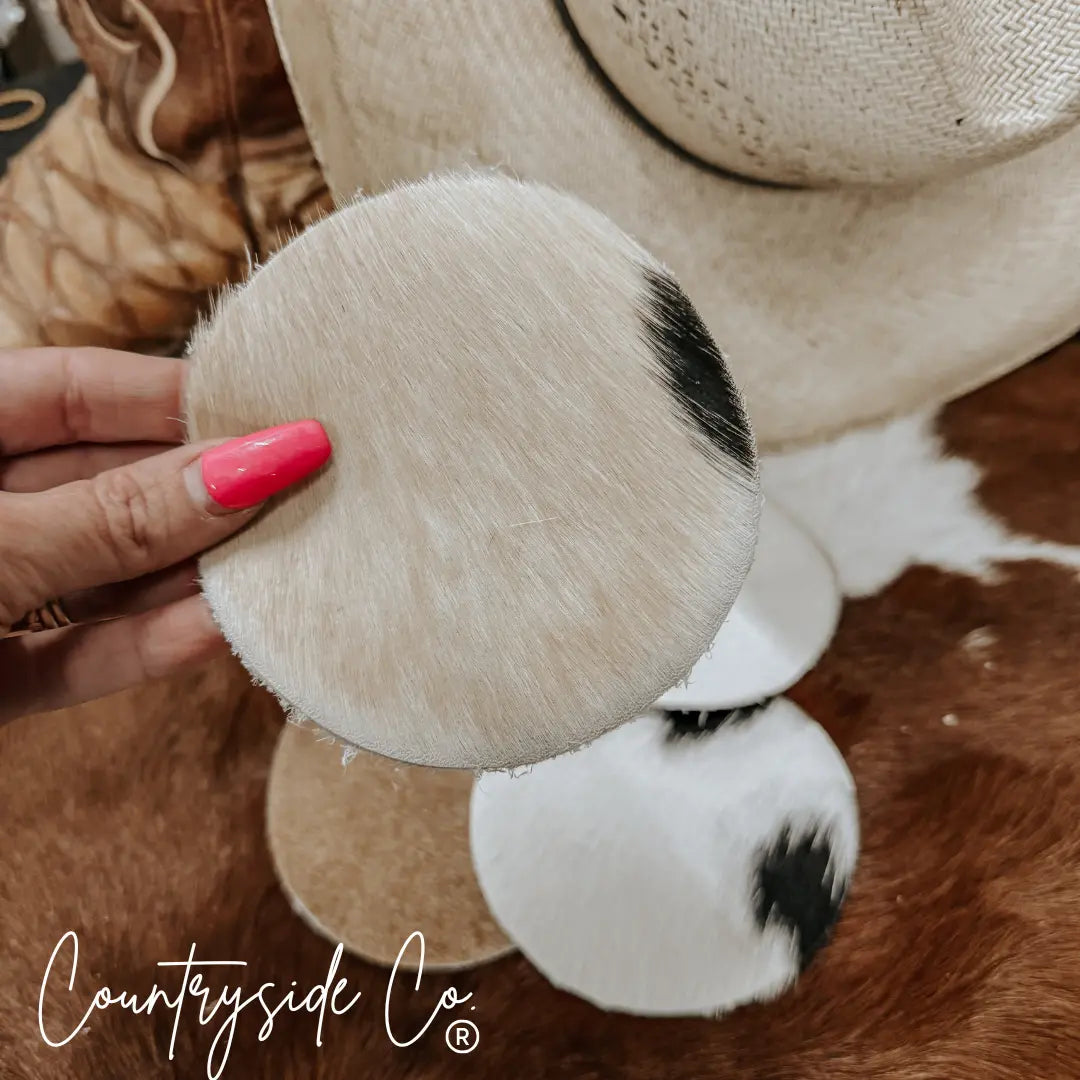 Cowhide coasters with black and white patterns, held by a hand with pink nail polish.