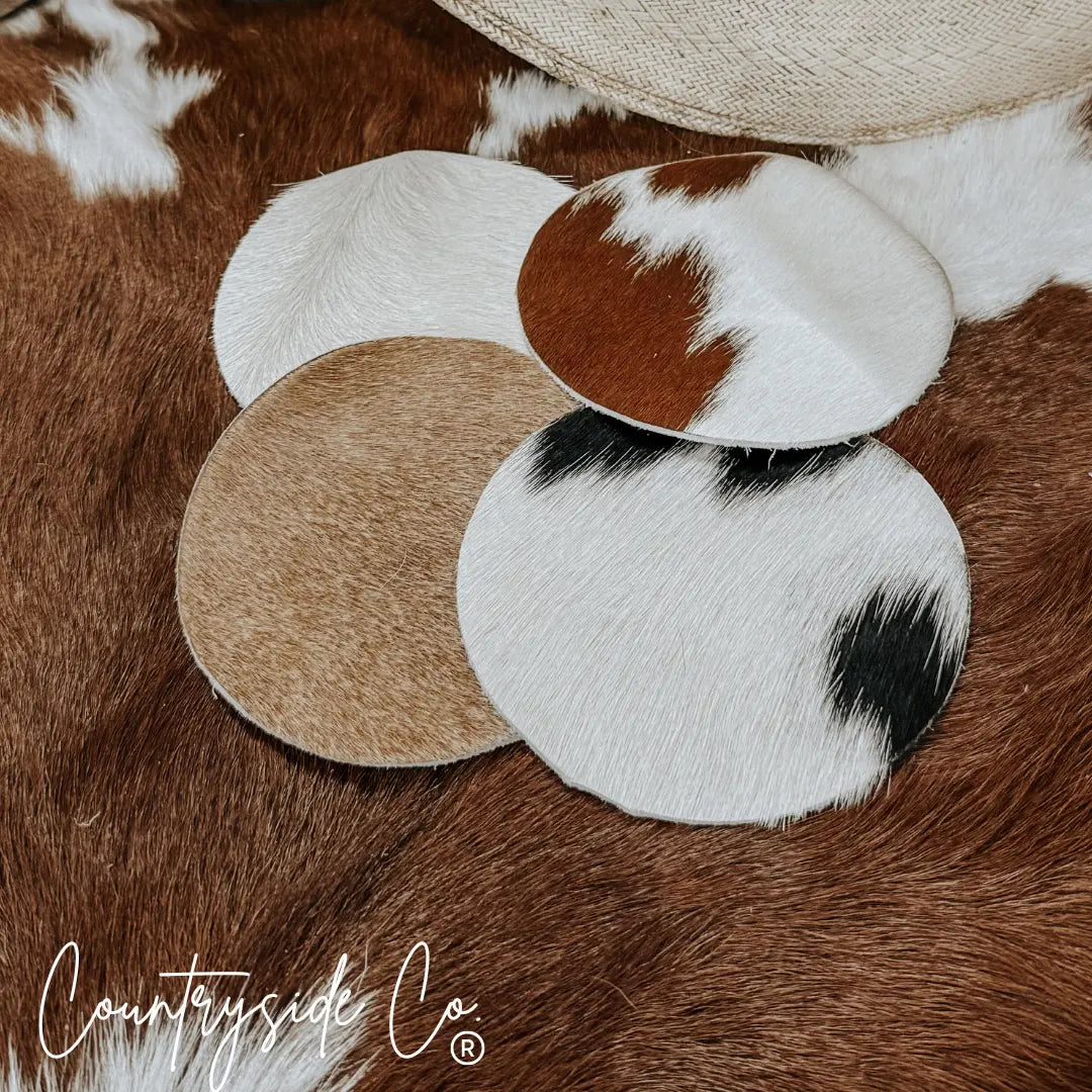 Round cowhide coasters with varied natural patterns in brown, white, and black.