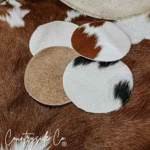 Round cowhide coasters with varied natural patterns in brown, white, and black.
