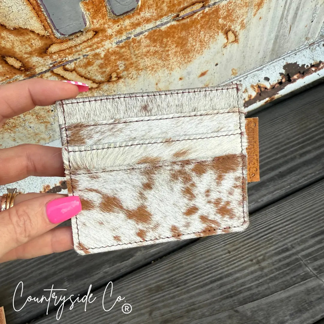 Cowhide credit card holder with "Countryside Co." tag on wooden surface