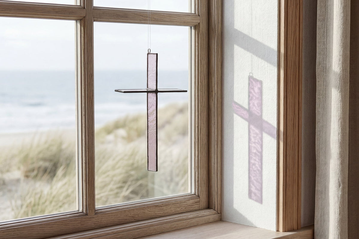 Warm Stone Cross Suncatcher hanging in a window and catching natural light