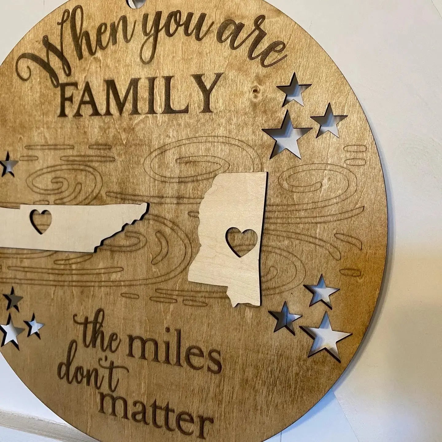 Round wood sign with "When you are family the miles don't matter" text, Tennessee and Mississippi outlines, and star cut-outs.