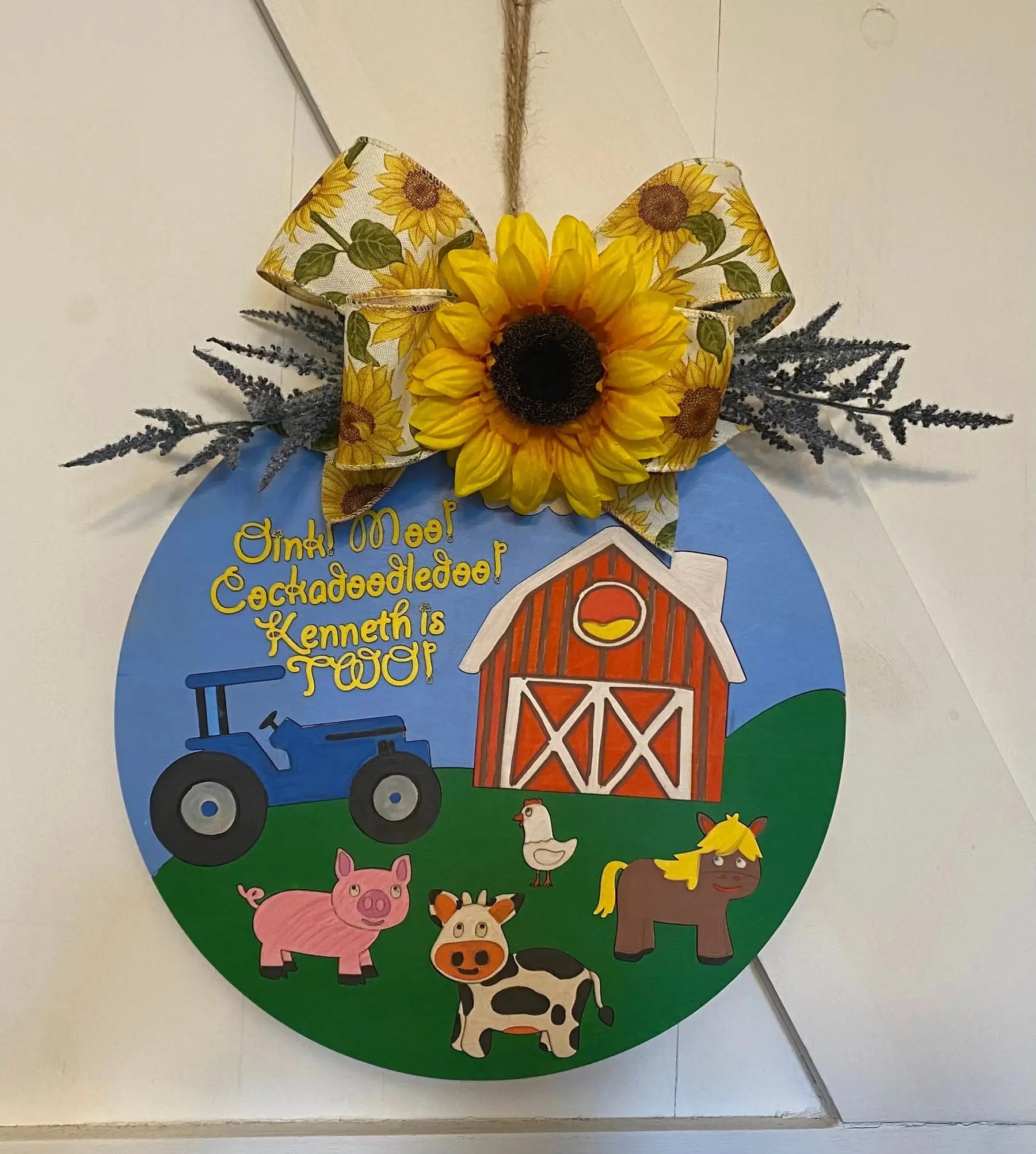 Round wood farm-themed sign with tractor, pig, cow, chicken, and barn, saying "Kenneth is Two!"