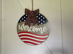 Round welcome sign with American flag design and patriotic bow.
