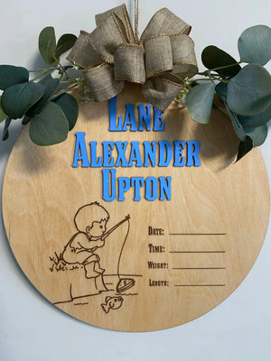 Personalized round wooden baby name sign with fishing graphic and stat lines.