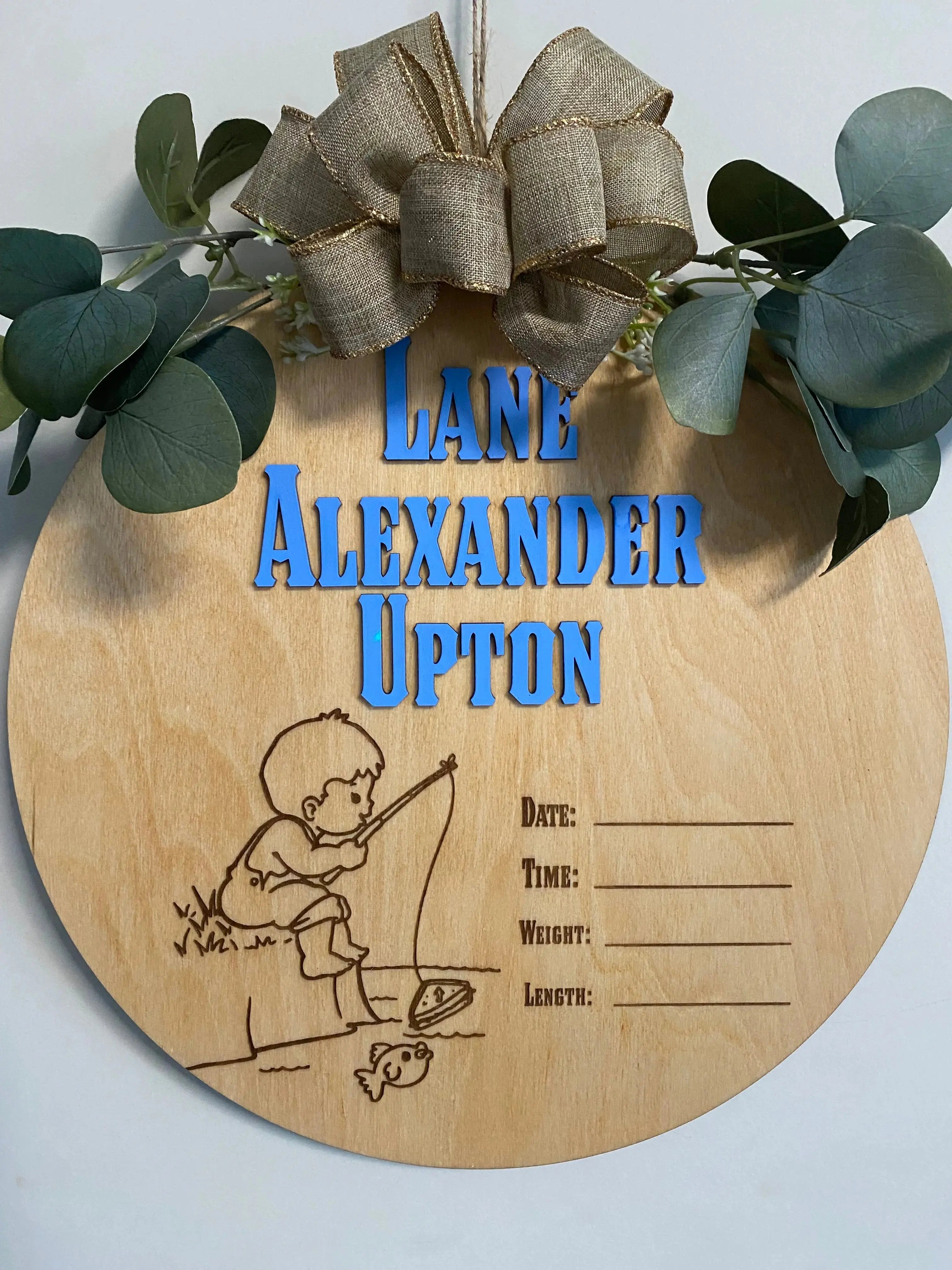 Personalized round wooden baby name sign with fishing graphic and stat lines.
