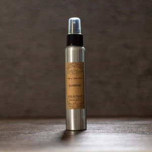 Dewdrop Mystique Daybreak Room and Linen Spray in a silver bottle with a brown label.