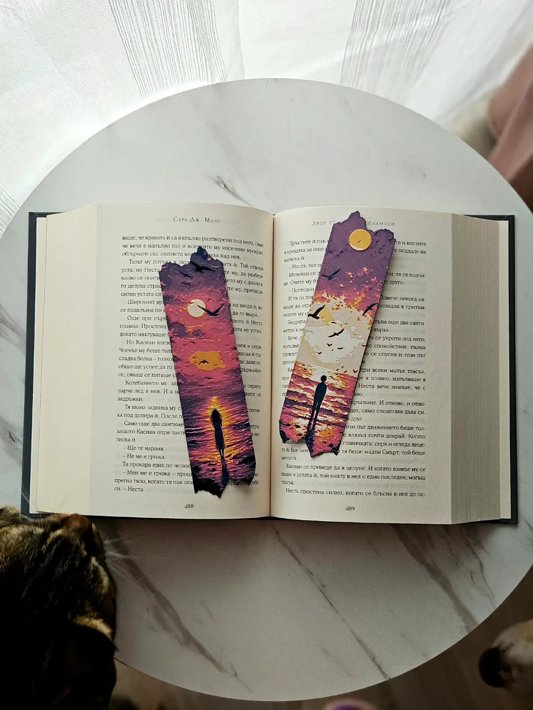 Open book with two sunset ocean bookmarks and a cat in the foreground.