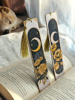 Celestial moon bookmarks with gold tassels on a book. Handmade crescent moon and floral design.