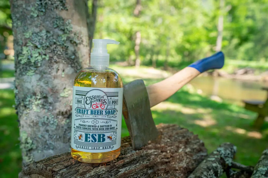Bottle of ESB Craft Beer Soap on wood logs with an axe in the background.
