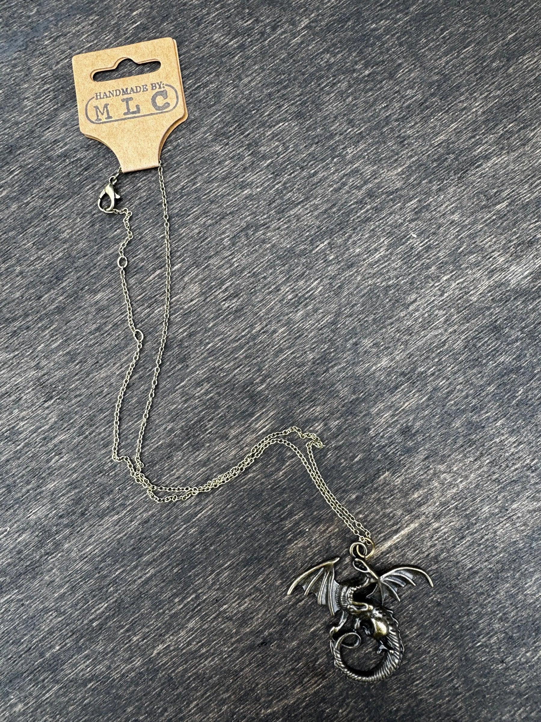 Bronze dragon necklace on gray background. Fantasy jewelry featuring a coiled wyrm pendant on a chain with a tag.