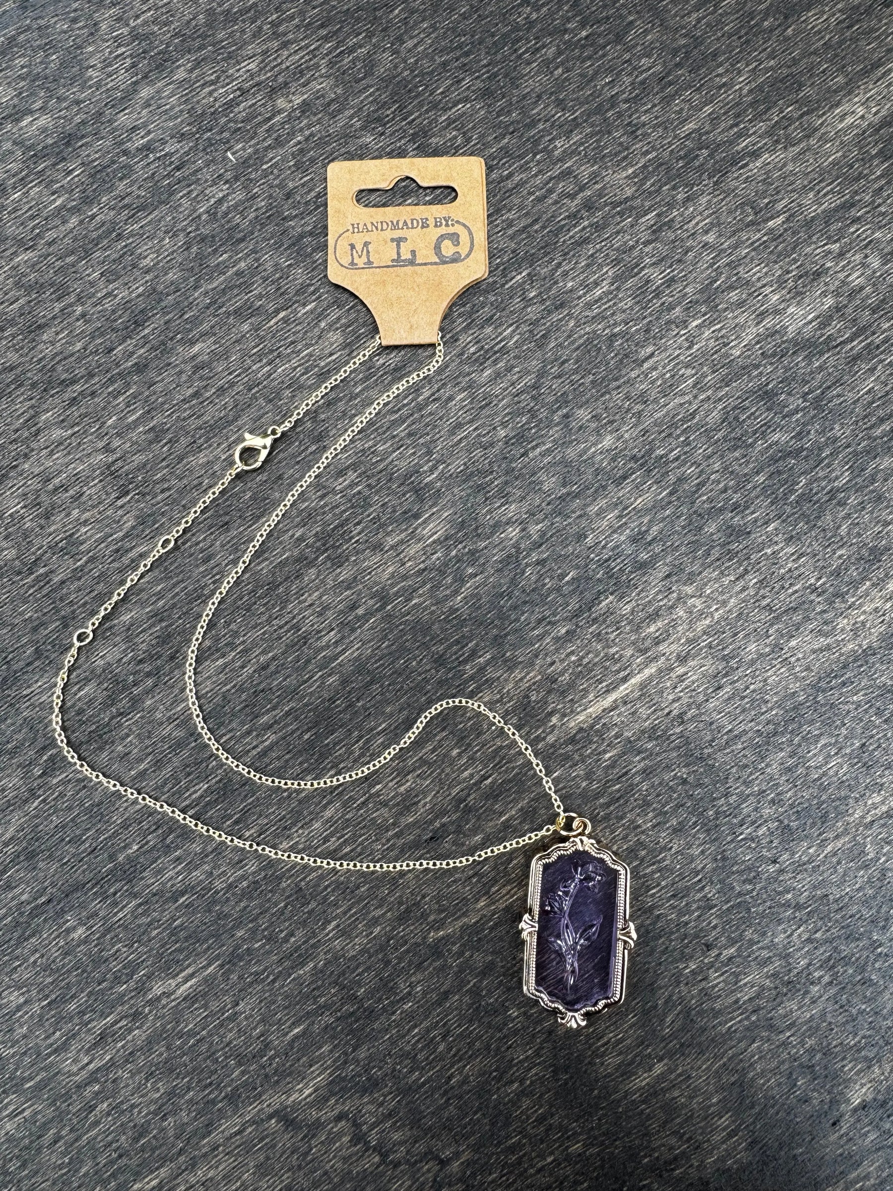 Purple glass necklace with a carved flower pendant and a silver chain. Tag reads "Handmade by: MLC".