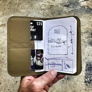 Tan fabric wallet holding a notebook with a sketch and cards, including a guitar image.