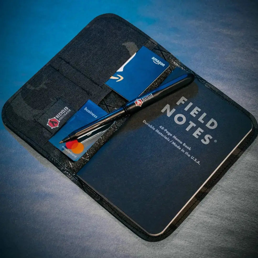 Field Notes wallet organizer with Amazon card, Mastercard, and pen on a dark blue surface.