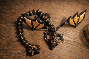 Black and gold articulated 3D printed dragon with wings on a wooden surface.