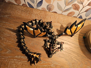 3D printed articulated dragon with black and gold wings.