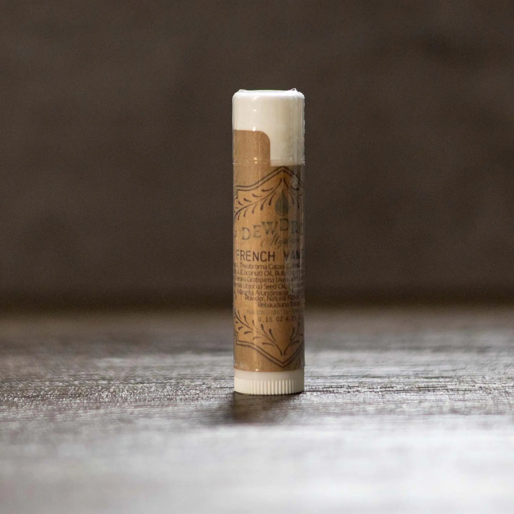 French Vanilla lip balm in brown paper tube with white cap and ingredient list, displayed on a textured surface.