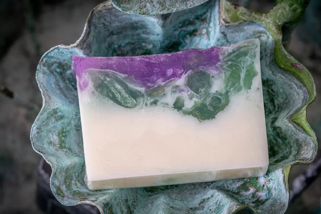 Goats milk soap slice with purple and green layers in a textured decorative dish.