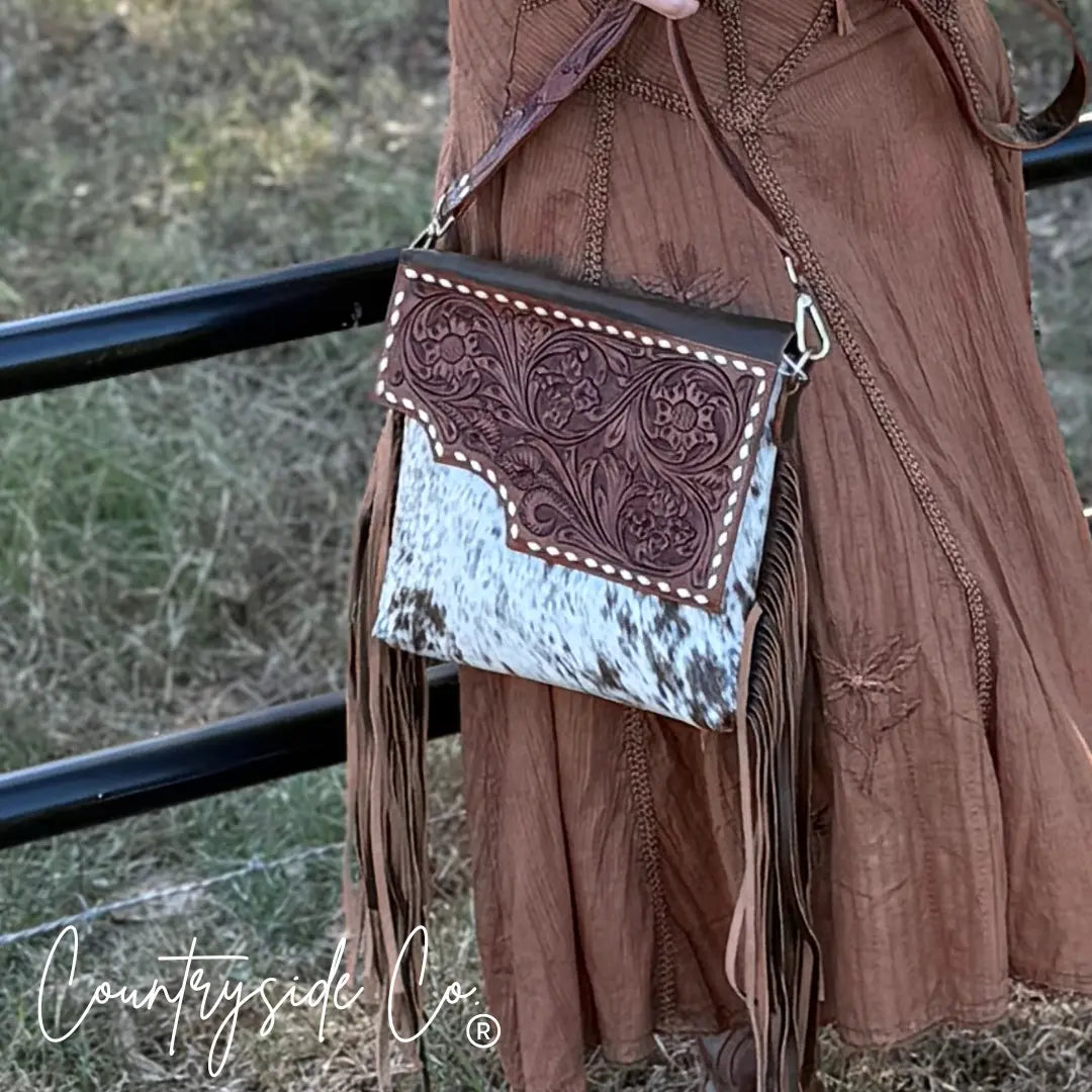 Tooled leather crossbody bag with cowhide front and fringe detail.