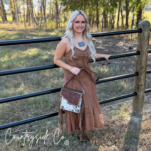 Woman wearing a brown dress holding a tooled leather and cowhide purse with fringe.