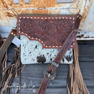 Tooled leather shoulder purse with cowhide front, fringe, and longhorn buckle.